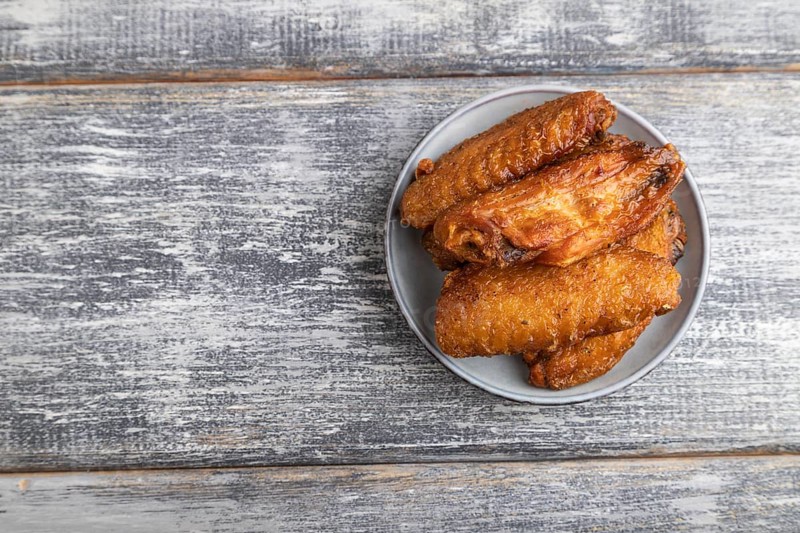 Fried chicken wings on a wooden plate on a gray wooden background. Top view, flat lay, close up, copy space