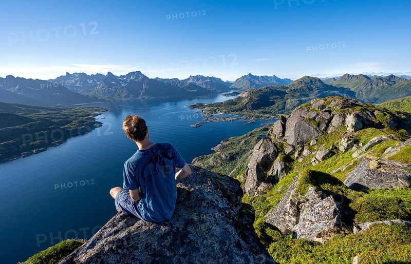 Mountaineer sitting on the summit of Dronningsvarden or Stortinden, behind mountains and fjord Raftsund, Sonnenstern, Vesteralen, Norway, Europe