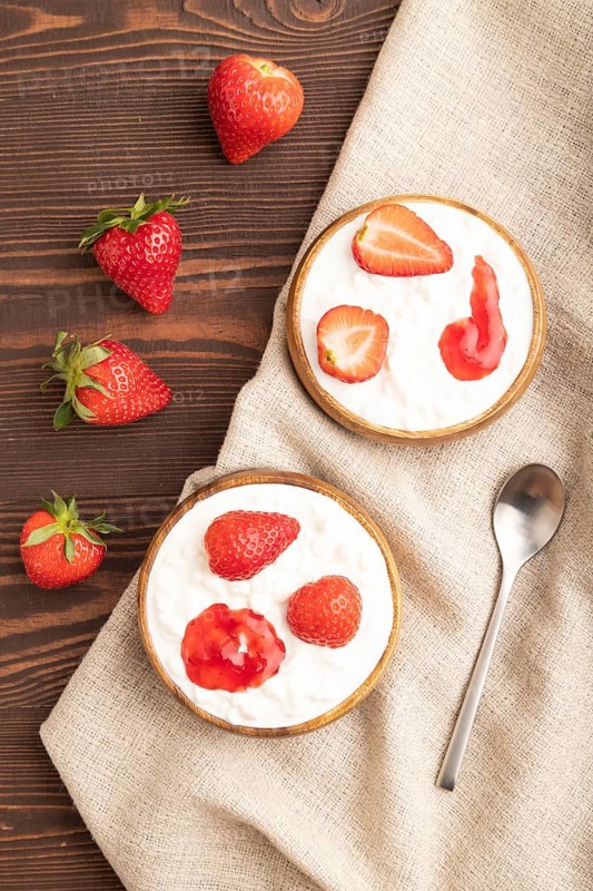 Grained cottage cheese with strawberry jam on brown wooden background and linen textile. top view, flat lay, close up