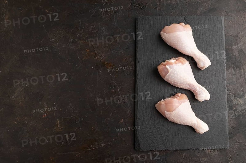 Raw chicken legs on a black slate cutting board on a black concrete background. Top view, flat lay, copy space