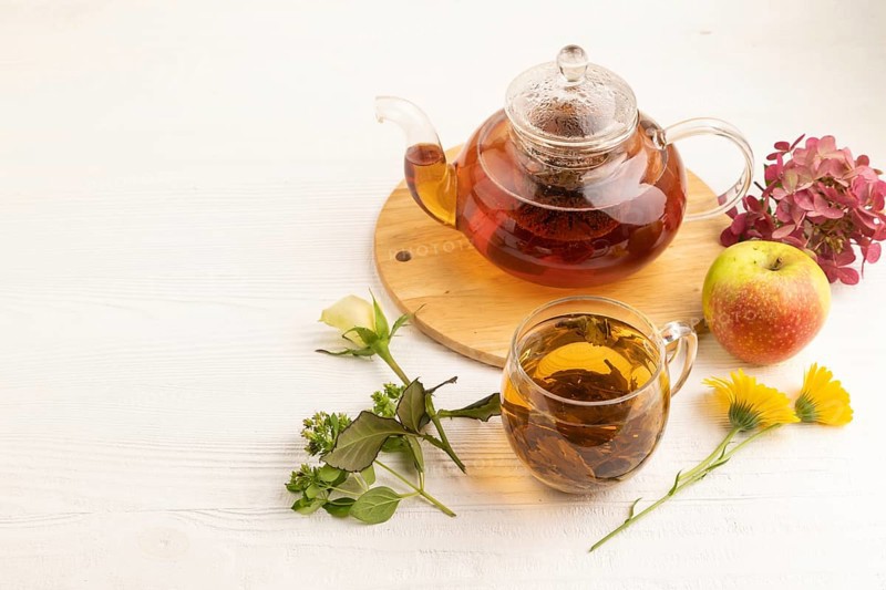 Red tea with herbs in glass teapot on white wooden background. Healthy drink concept. Top view, flat lay, copy space