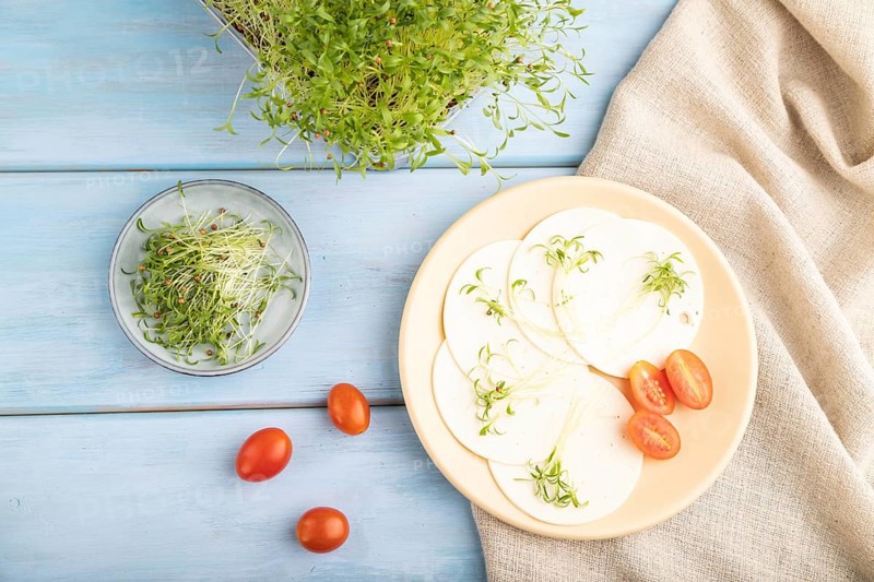 White cheese with tomatoes and cilantro microgreen on blue wooden background and linen textile. top view, flat lay, close up