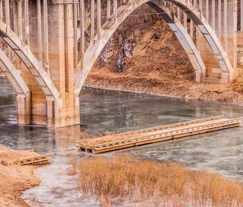 Arch bridge with columns spanning a river with a smaller bridge with pieces missing in South Korea