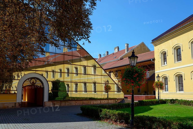 A yellow building reflected in a large glass facade, flanked by trees and a paved path, Officers' Palace, Komarno, Komarom, Komorn, Nitriansky kraj, Slovakia, Europe