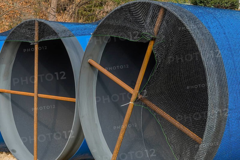 Closeup of large blue sections of steel industrial pipes sitting at construction site