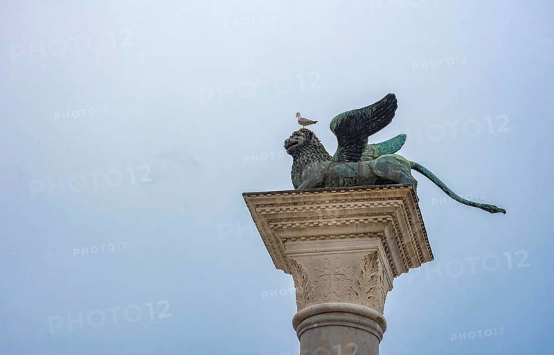 Winged lion of Saint Mark, old bronze statue on a column in San Marco square, famous tourist attraction in Venice. Italy