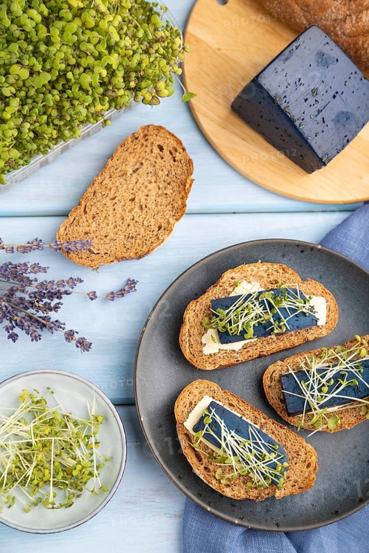Bread sandwiches with blue lavender cheese and mustard microgreen on blue wooden background and linen textile. top view, flat lay, close up