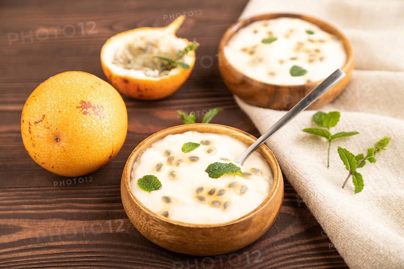Yoghurt with granadilla and mint in wooden bowl on brown wooden background and linen textile. side view, close up, selective focus