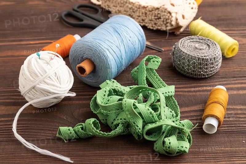Sewing accessories: scissors, thread, thimbles, braid on brown wooden background. Side view, close up