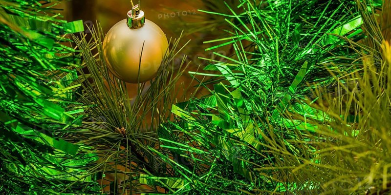 Closeup of gold Christmas ornament and green tensile garland hanging on pine tree in local park in South Korea
