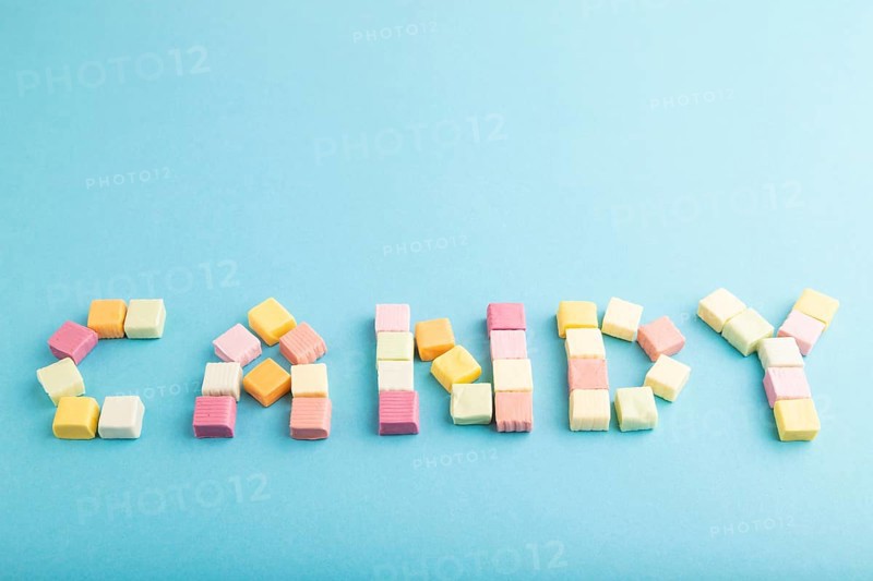 The inscription candy laid out with various fruit jelly chewing candies on blue pastel background. apple, banana, tangerine, side view, copy space