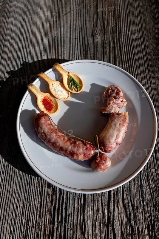 A Plate with Luganighe Sausage and with Species in Spoon Like Saffron and Parmesan Cheese and Rosemary on a Plate on a Wood Table with Sunlight in Switzerland