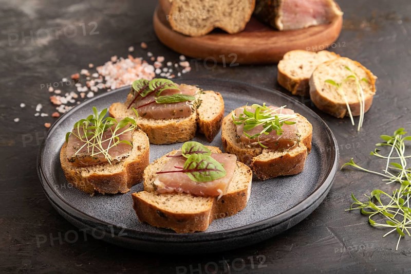 Bread sandwiches with jerky salted meat, sorrel and cilantro microgreen on black concrete background. side view, close up