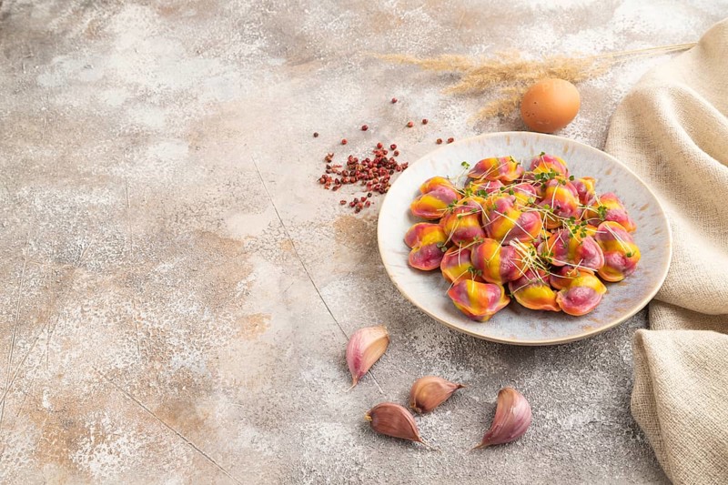 Rainbow colored dumplings with pepper, herbs, microgreen on brown concrete background and linen textile. Side view, copy space