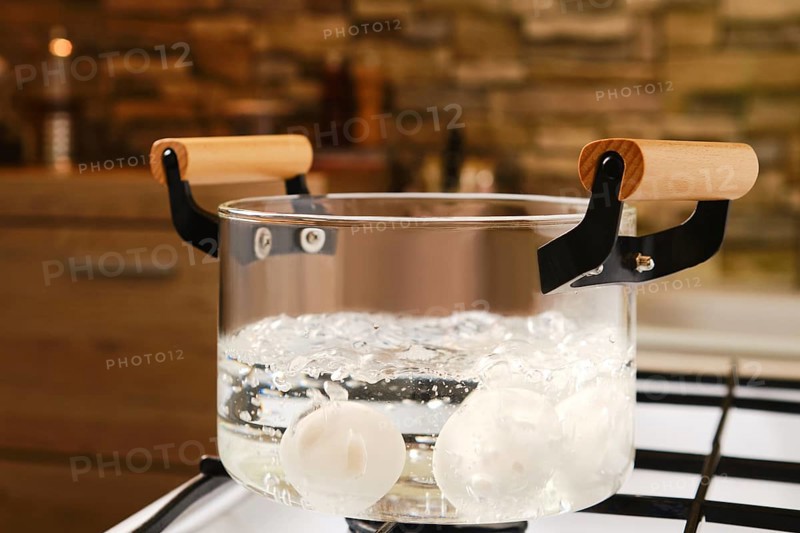 Closeup view of transparent glass saucepan with boiling eggs on a gas stove