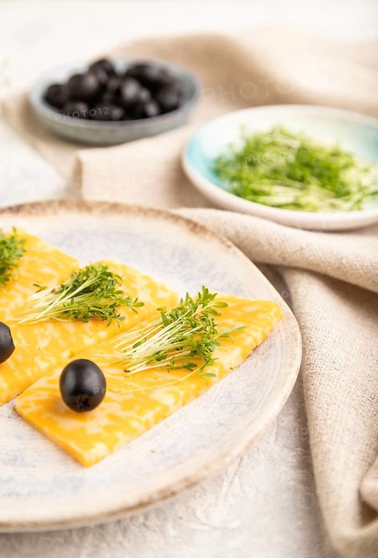 Marble cheese with olives and watercress microgreen on gray concrete background and linen textile. side view, close up, selective focus