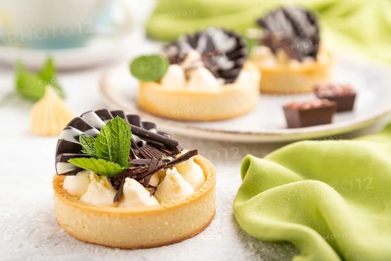 Sweet tartlets with chocolate and cheese cream with cup of coffee on a gray concrete background and green textile. Side view, close up, selective focus