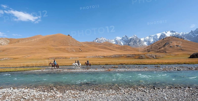 Riders on horses on the river bank, mountain landscape with yellow meadows and river Kol Suu, mountain peak with glacier, hike to the mountain lake Kol Suu, Keltan Mountains, Sary Beles Mountains, Tien Shan, Naryn Province, Kyrgyzstan, Asia