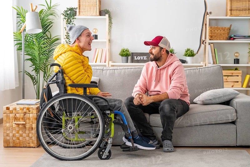 Disabled man in wheelchair and friends chatting relaxed in the living room of the house