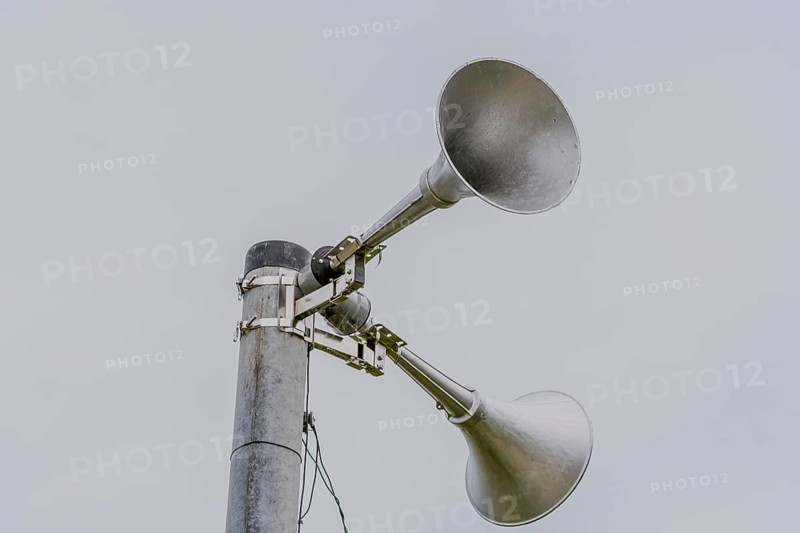Large metal loud speakers used for emergency warnings mounted on top of metal pole against gray sky