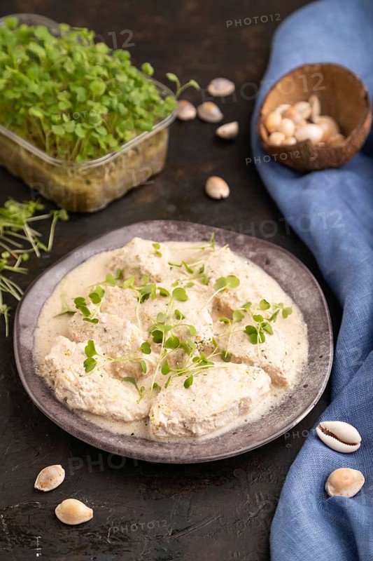Stewed chicken fillets with coconut milk sauce and rucola microgreen on black concrete background and blue linen textile. side view, close up, selective focus