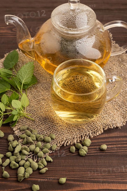 Green oolong tea with herbs in glass on brown wooden background and linen textile. Healthy drink concept. Side view, close up