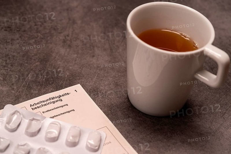 A cup of tea next to medication and a certificate of incapacity for work on a grey background
