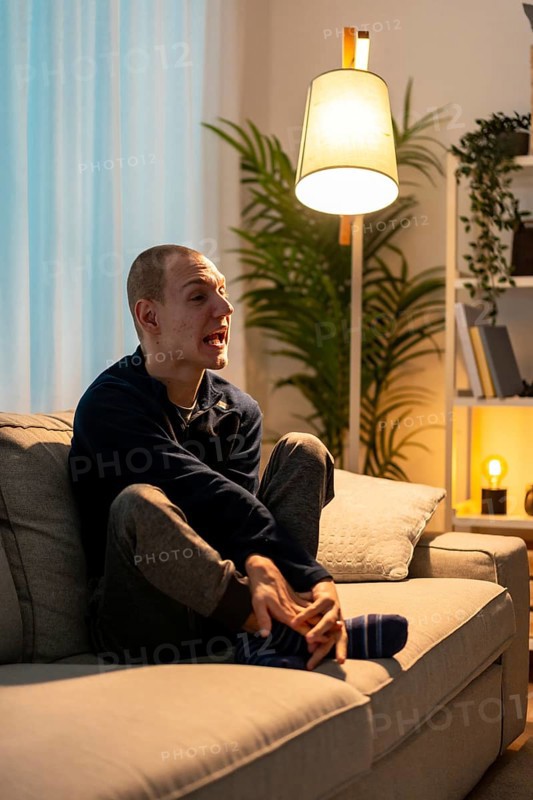 Vertical photo of a sad disabled man sitting on the sofa alone at home