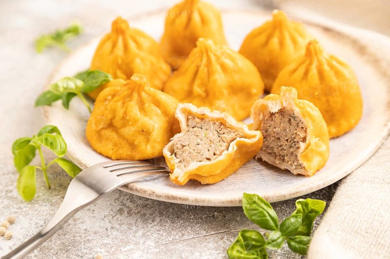 Fried manti dumplings with pepper, basil on gray concrete background and linen textile. Side view, close up, selective focus