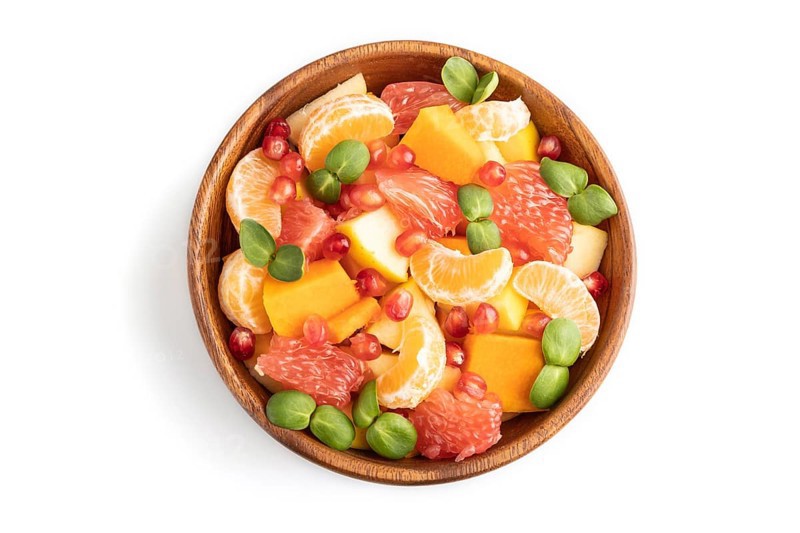 Vegetarian fruit salad of pumpkin, tangerine, pomegranate, grapefruit, sunflower microgreen sprouts isolated on white wooden background. Top view, flat lay, close up