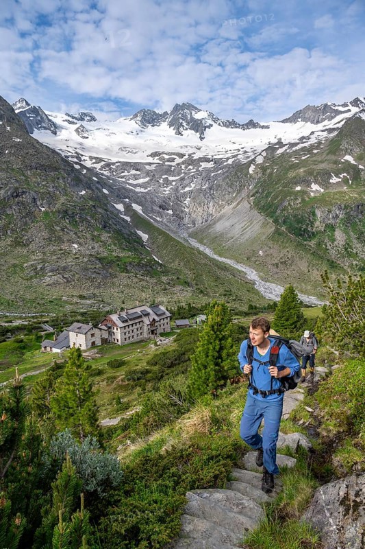 Two mountaineers on a hiking trail in a picturesque mountain landscape with alpine roses, in the background mountain peak Grosser Moeseler with glacier Waxeggkees and mountain hut Berliner Huette, Berliner Hoehenweg, Zillertal Alps, Tyrol, Austria, Europe