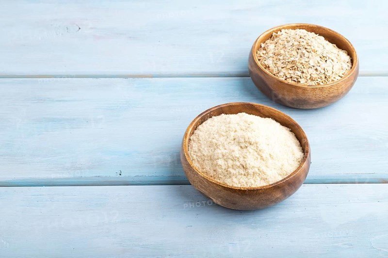 Powdered milk and oatmeal baby food mix, infant formula on blue wooden background. Side view, copy space, artificial feeding concept