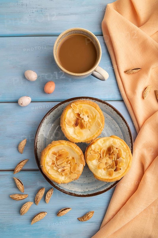 Traditional portuguese cakes pasteis de nata, custard small pies with almonds with cup of coffee on blue wooden background and orange textile. Top view, flat lay