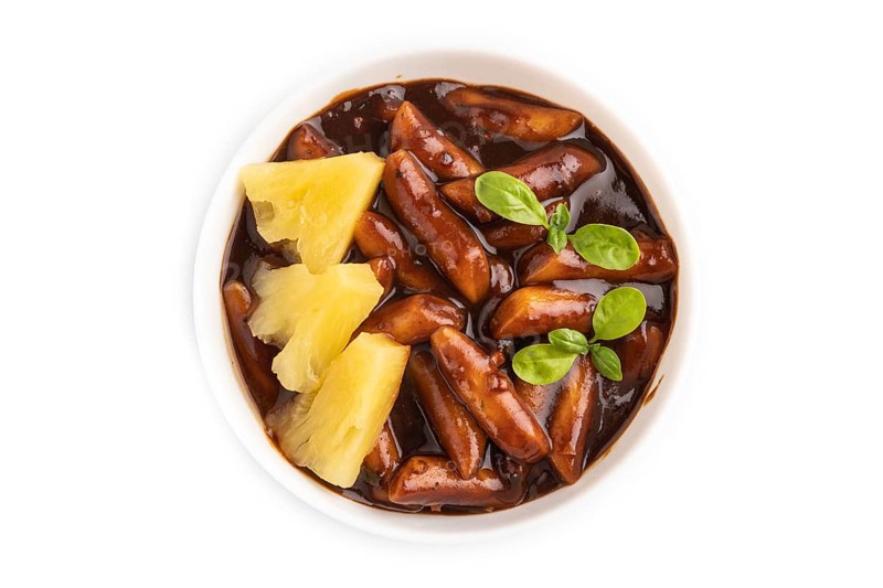 Tteokbokki or Topokki, fried rice cake stick, popular Korean street food with spicy jjajang sauce and pineapple isolated on white background. Top view, flat lay
