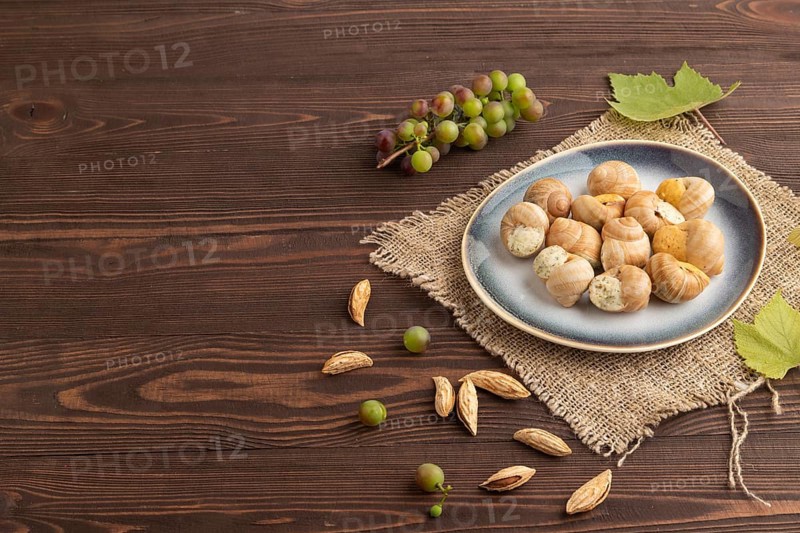Grape (Burgundy) snails with butter and cheese on brown wooden background and linen textile. Side view, copy space