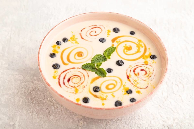 Yoghurt with bilberry and caramel in ceramic bowl on gray concrete background. side view, close up