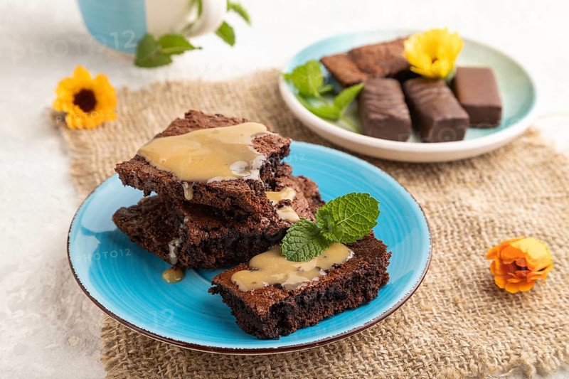 Chocolate brownie with caramel sauce with a cup of coffee on gray concrete background and linen textile. side view, close up