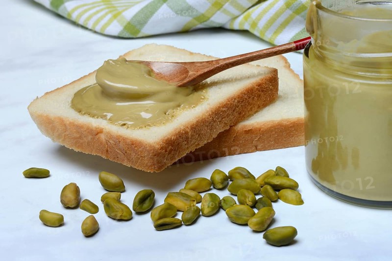 Pistachio cream with spoon on slices of bread, pistachio