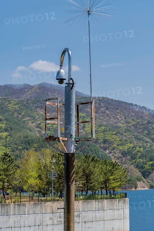Round closed circuit camera on curved pole with lake and mountain under blue sky in background