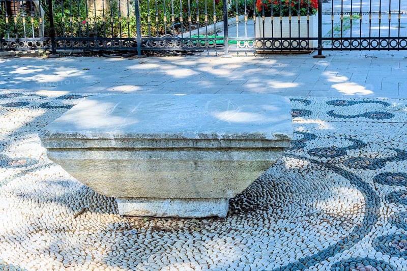 Concrete park bench on design of pebbles beside walkway under shade tree in Istanbul, Tuerkiye