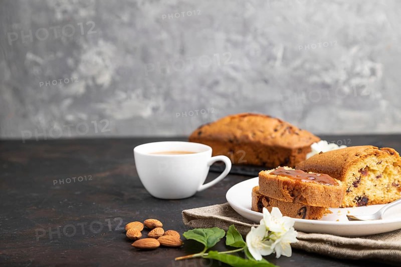Homemade cake with raisins, almonds, soft caramel and a cup of coffee on a black concrete background and linen textile. Side view, copy space, selective focus