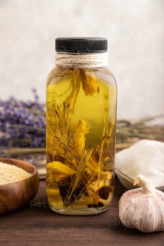 Sunflower oil in a glass jar with various herbs and spices, lavender, sesame, rosemary on a brown wooden background. Side view, close up