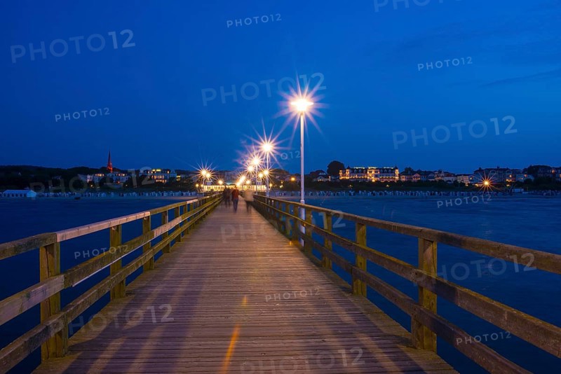 Nocturnal pier with illuminated street lamps and star effect, illuminated pier with strolling people and buildings, quiet, late evening mood, night on the beach with calm waves in deep twilight, clear, blue sky, star effect on the lanterns, motion blur, wipe effect, long exposure, view from the seaside to Ahlbeck, seaside resort, Usedom Island, Mecklenburg-Western Pomerania, Germany, Europe