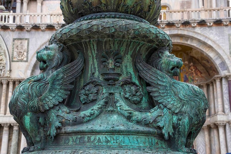 Old street ornament with winged lions and San Marco Basilica in the background, in St. Mark Square, famous tourist attraction in Venice, Italy. Selective focus