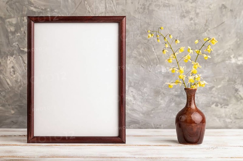 Wooden frame with yellow barrenwort flowers in ceramic vase on gray concrete background. side view, copy space, still life, mockup, template, spring, summer minimalism concept
