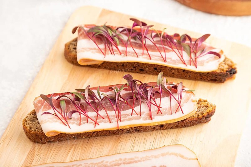 Bread sandwiches with jerky salted meat and lard with beet microgreen on gray concrete background. side view, close up, selective focus