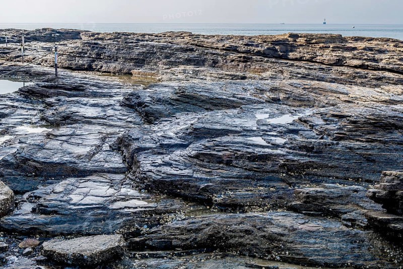 Stratified geological rocks with layers of various shapes with ocean in background in South Korea