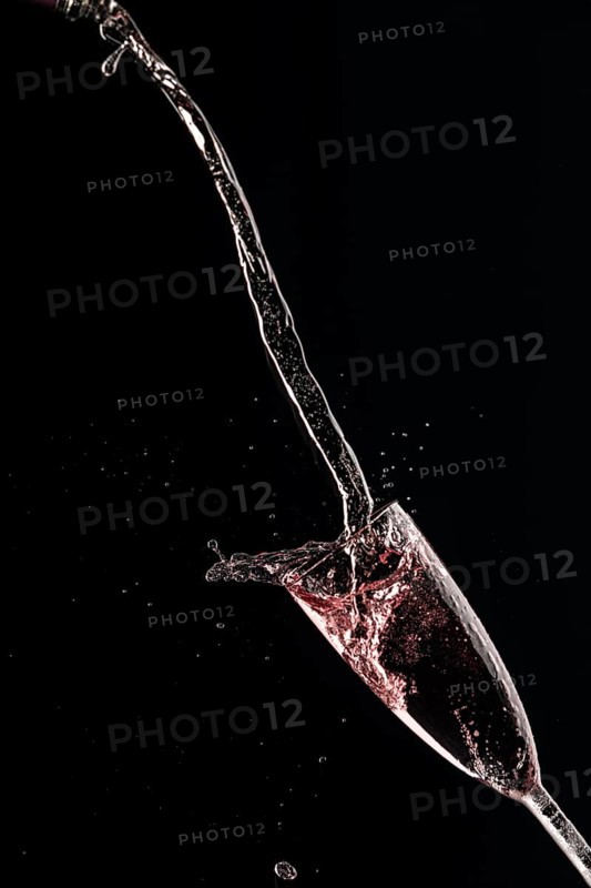 Rose champagne pours in an arc into a champagne glass on a black background