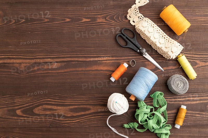 Sewing accessories: scissors, thread, thimbles, braid on brown wooden background. Top view, flat lay, copy space