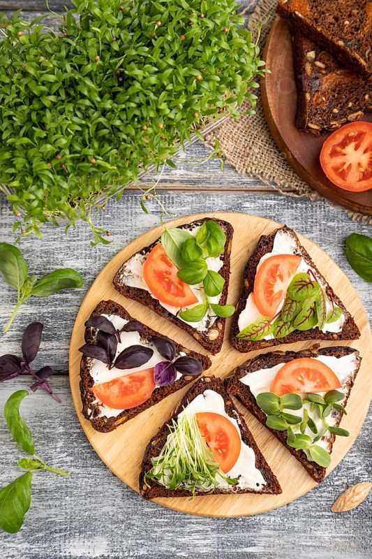 Grain rye bread sandwiches with cream cheese, tomatoes and cilantro microgreen on gray wooden background and linen textile. top view, flat lay, close up